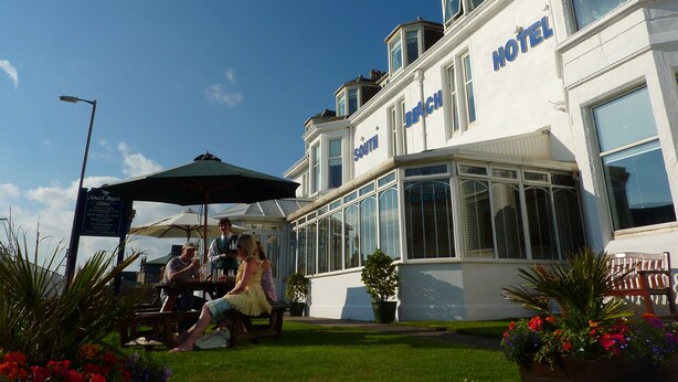A hotel with a large bay window, outdoor seating, and a sign indicating it is a restaurant. - The South Beach Hotel (Troon)