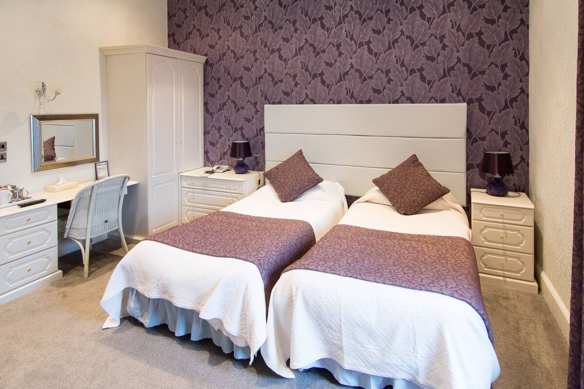 A hotel room with two beds, a desk, a wardrobe, and a mirror.
