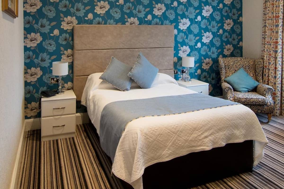 A bedroom with a large bed, a nightstand, a chair, and a patterned wall.