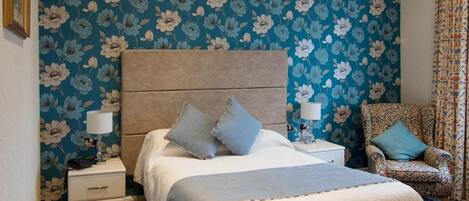 A bedroom with a large bed, a nightstand, a chair, and a patterned wall.