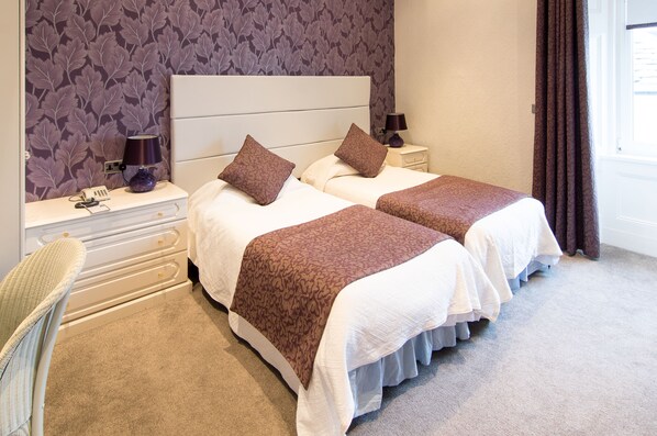 A hotel room with two beds, a nightstand with a lamp, a chair, and a patterned wallpaper. - The South Beach Hotel (Troon)