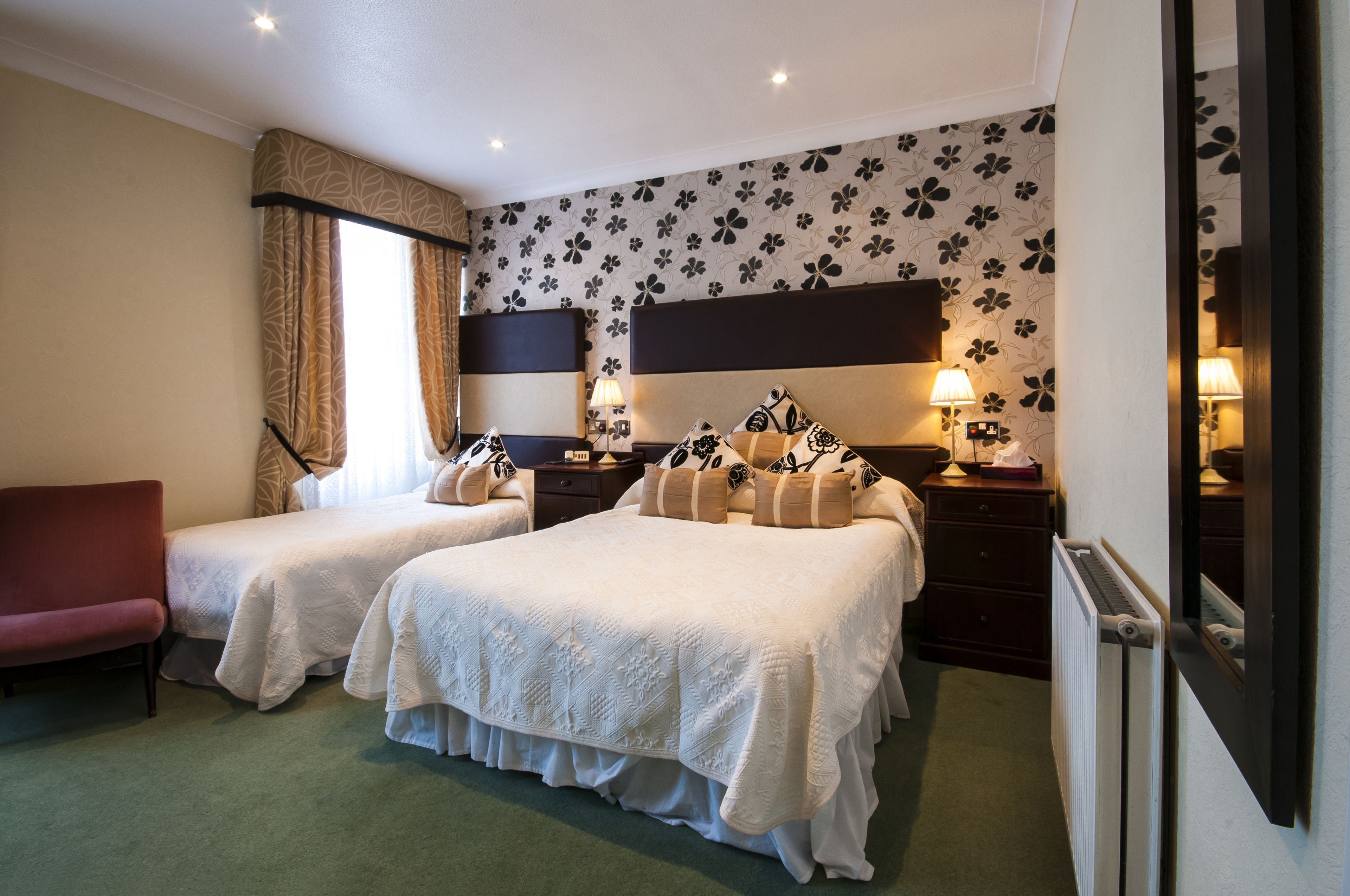 A hotel room with two beds, a red chair, a dresser, and a large mirror.