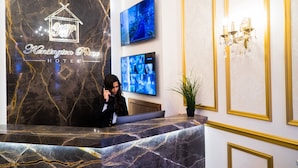 A hotel reception desk with a marble countertop and a receptionist. - Kensington Prime Hotel (London)