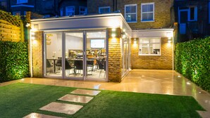 A modern house with a glass-enclosed patio, a brick exterior, and a well-maintained lawn. - Kensington Prime Hotel (London)