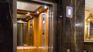An elevator interior with a wooden finish and a marble wall. - Kensington Prime Hotel (London)
