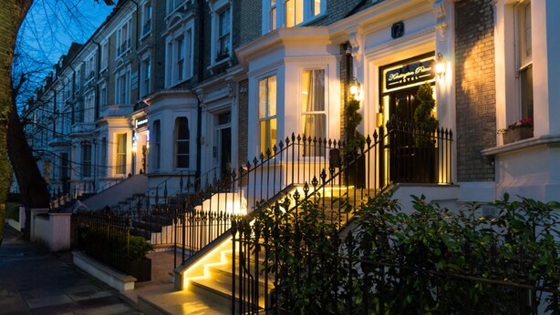 A row of Victorian-style townhouses with a well-lit entrance and a visible hotel sign. - Kensington Prime Hotel (London)