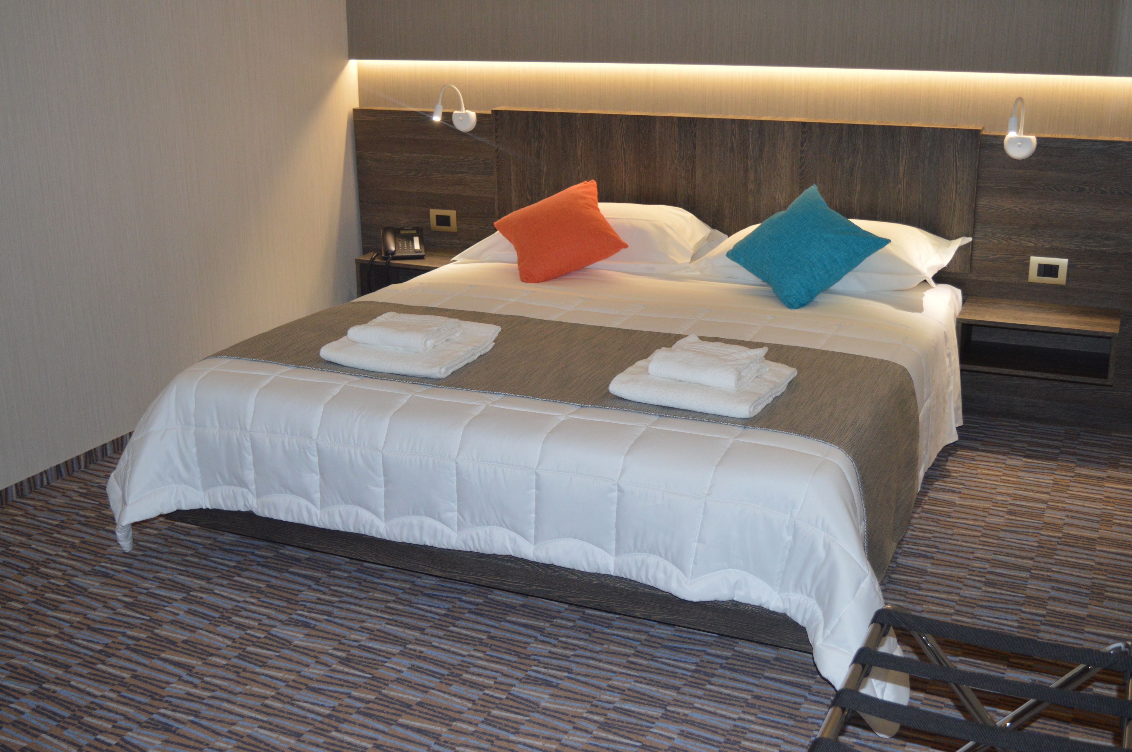 Habitación de hotel con una cama bien hecha, un cabecero de madera y una mesita de noche con un teléfono.