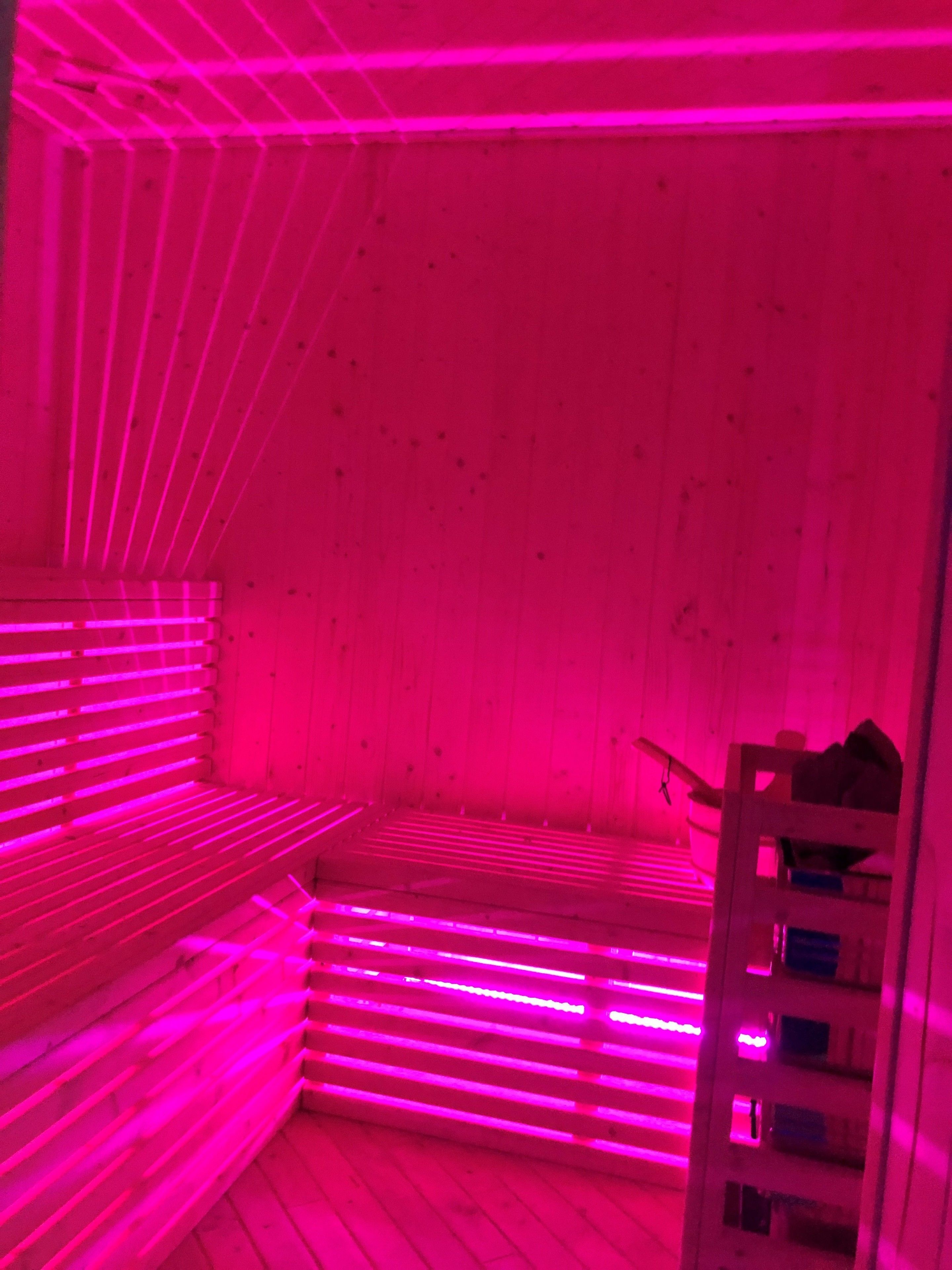 A room with pink lighting, wooden walls, and a bunk bed.
