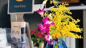 Una reception hotel con un display digitale per le recensioni degli ospiti, un vaso di fiori e un porta cartelli in plastica trasparente.