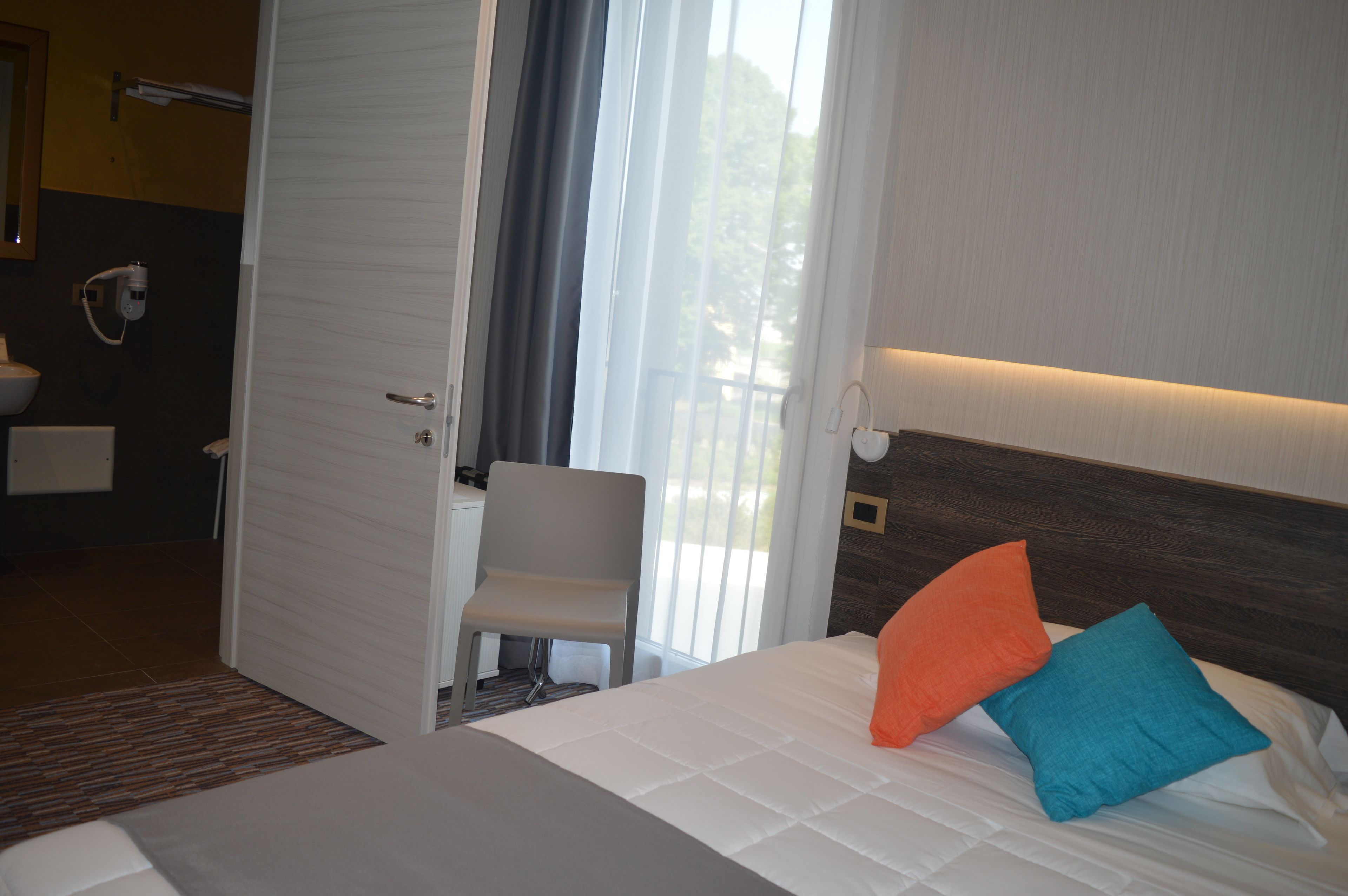 A hotel room with a bed, a chair, a bathroom, and a window with curtains.