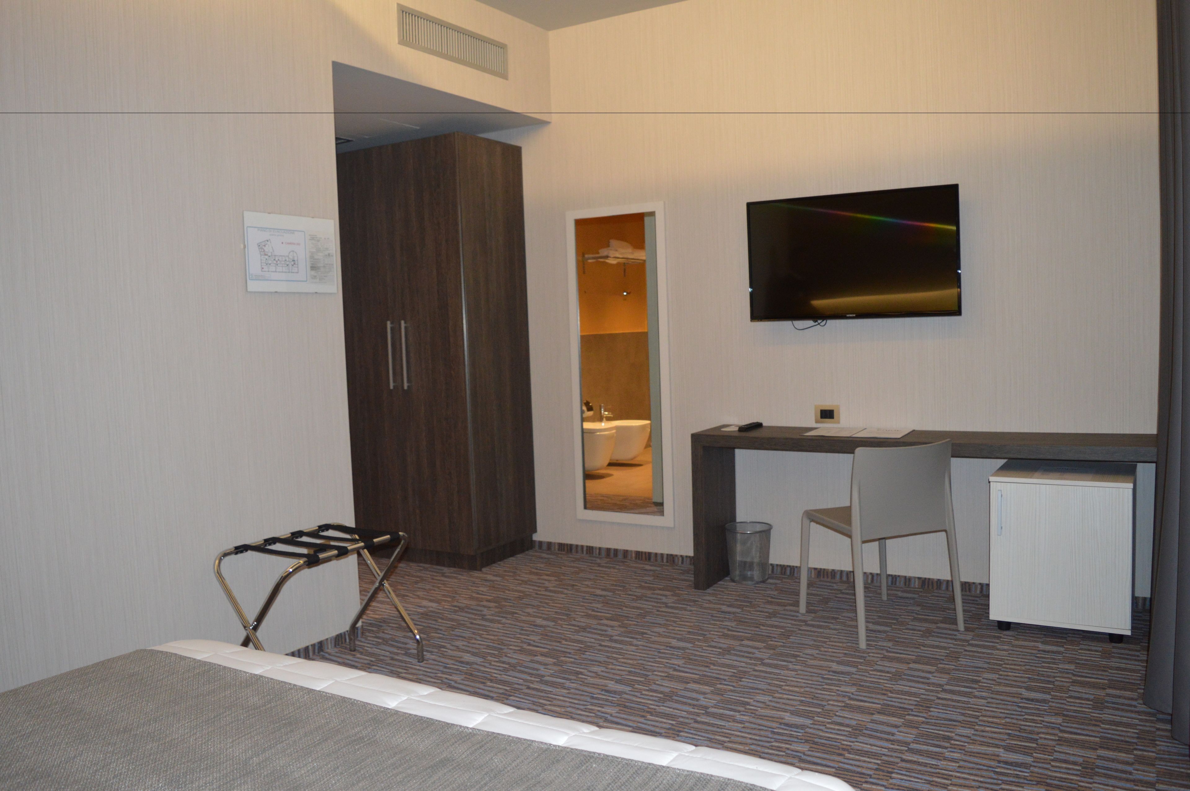 Ein Hotelzimmer mit Bett, Schreibtisch, Stuhl, Fernseher und einem durchgehenden Türspalte sichtbaren Badezimmer.