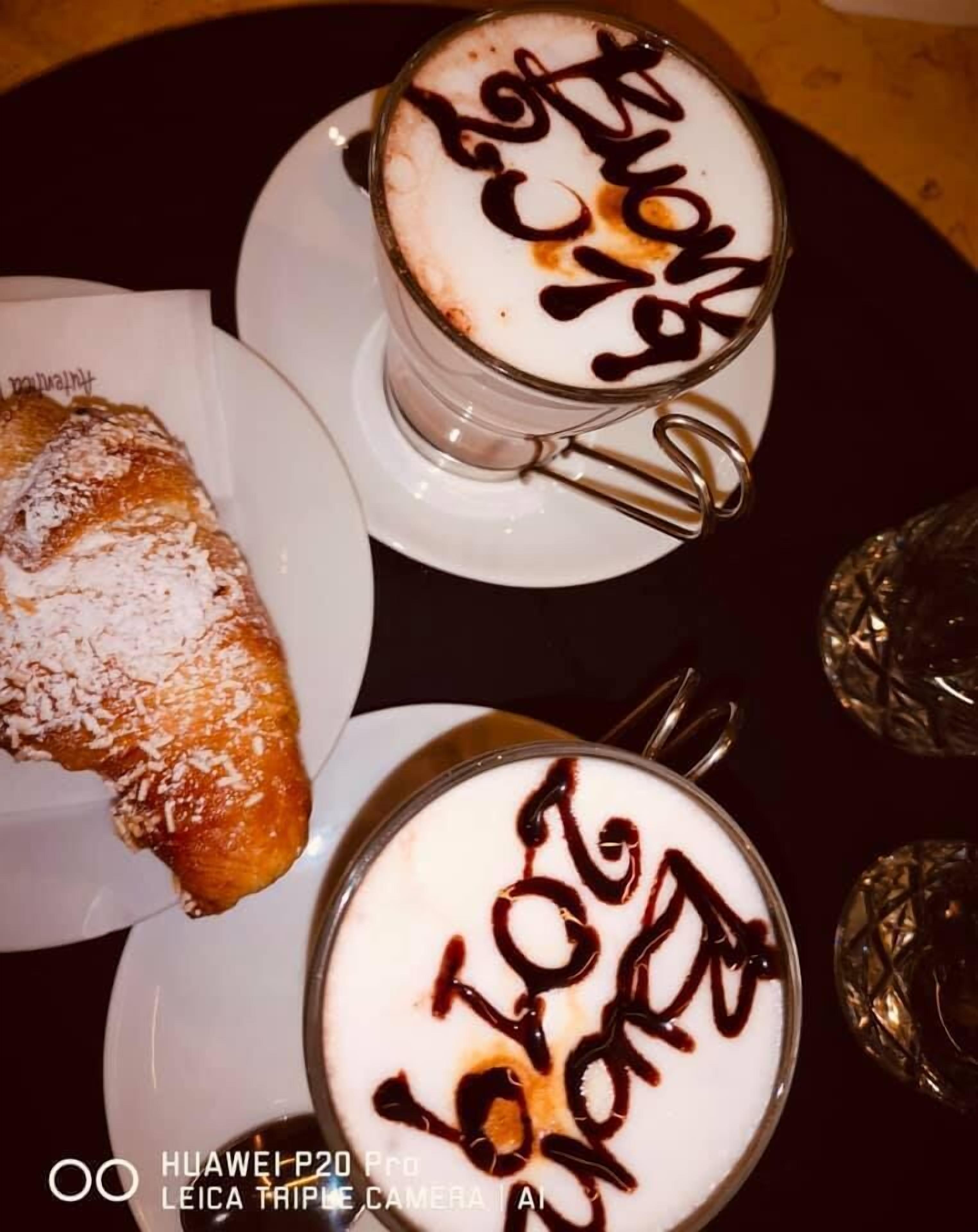 Zwei Tassen Kaffee mit Schokoladenglasur und ein Gebäck auf einem Teller.