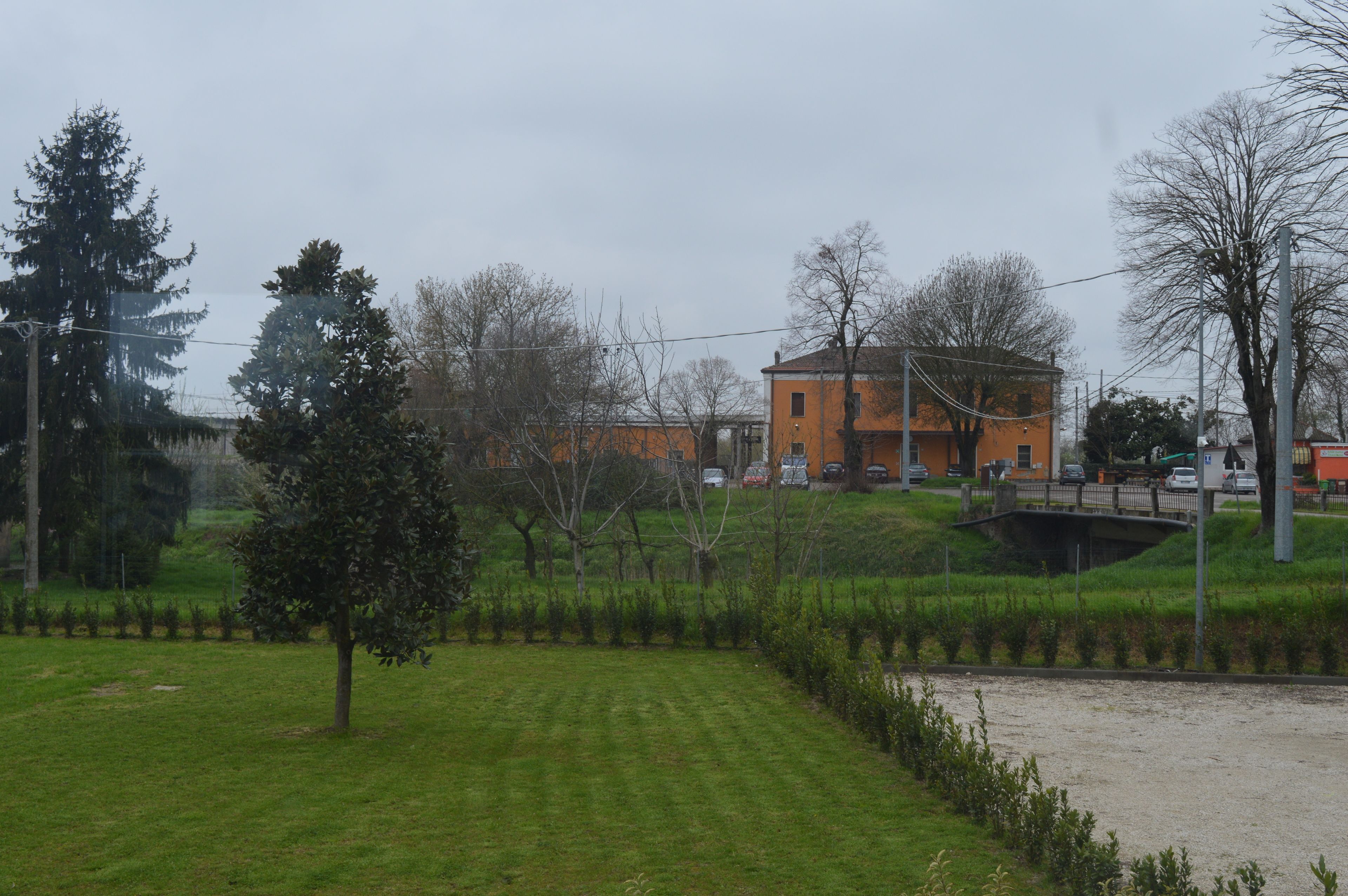 A building with a brick facade and a flat roof, surrounded by a grassy area with trees and a small bridge.