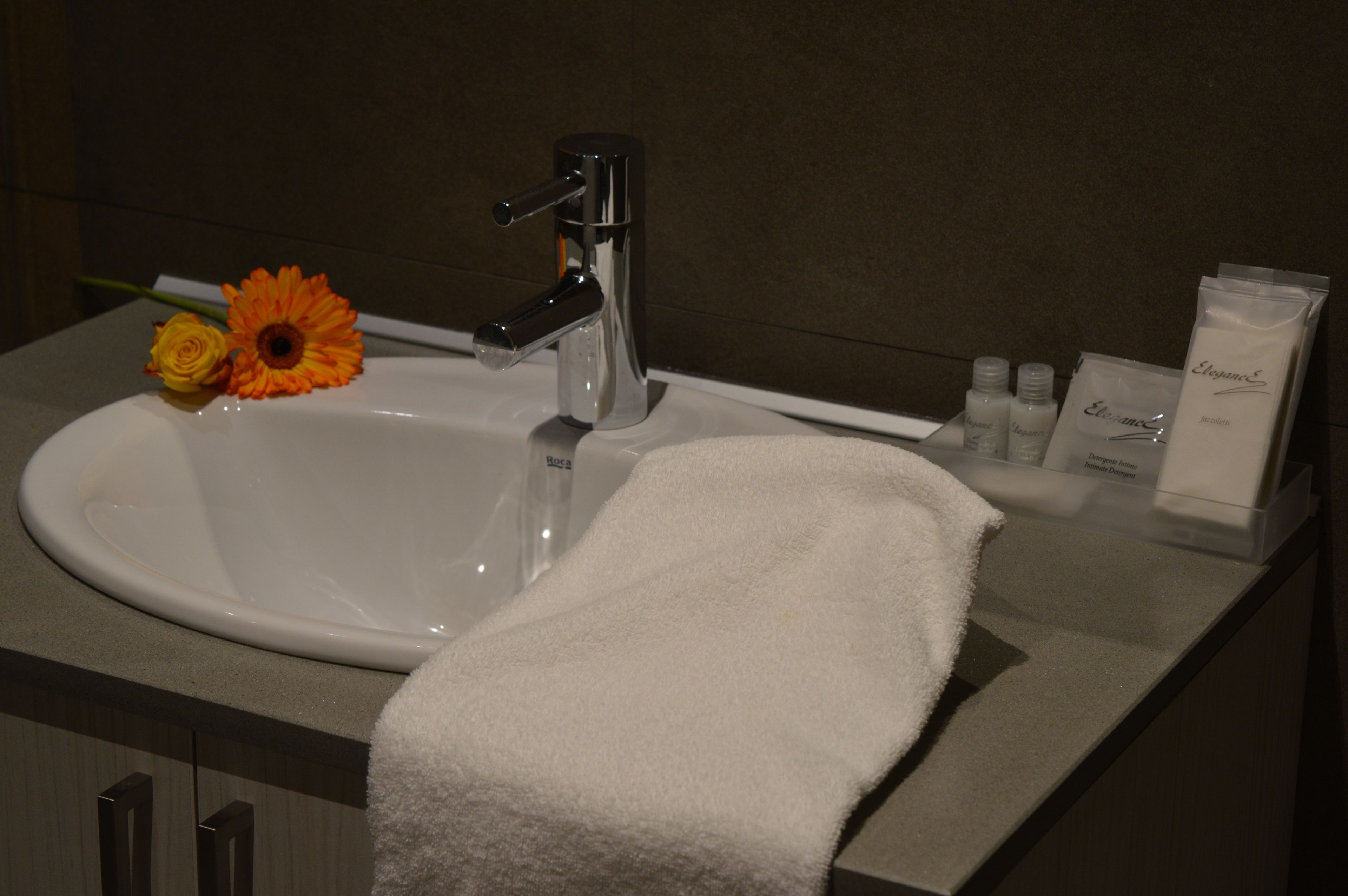 A bathroom sink with a white towel, a flower, and toiletries.
