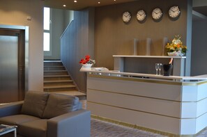 A reception area with a reception desk, a staircase, and a seating area with a couch. - Hotel Enjoy (Polesella)