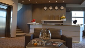 En moderne lobby med en lædersofa, en glaskrukke med dekorative genstande og et skilt med teksten 'ENJOY' på et bord.