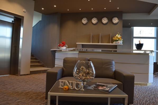 Un moderno vestíbulo de hotel con un sofá de cuero, un cuenco de vidrio con objetos decorativos y un cartel que dice 'ENJOY' sobre una mesa.