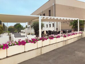 An outdoor seating area with white wicker furniture and a row of flower planters. - Hotel Enjoy (Polesella)