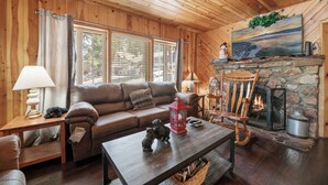 A cozy living room with a stone fireplace, wooden walls, a sofa, a coffee table, and a television mounted above the fireplace.