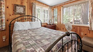 A wooden-paneled bedroom with a bed, a nightstand, a window with blinds, and a fan.