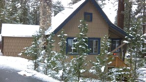 A two-story house with a stone chimney, wooden siding, and a gabled roof.