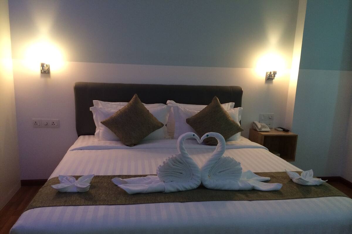 A hotel room with a neatly made bed, two pillows, a bedside table with a phone, and a wall-mounted light fixture.