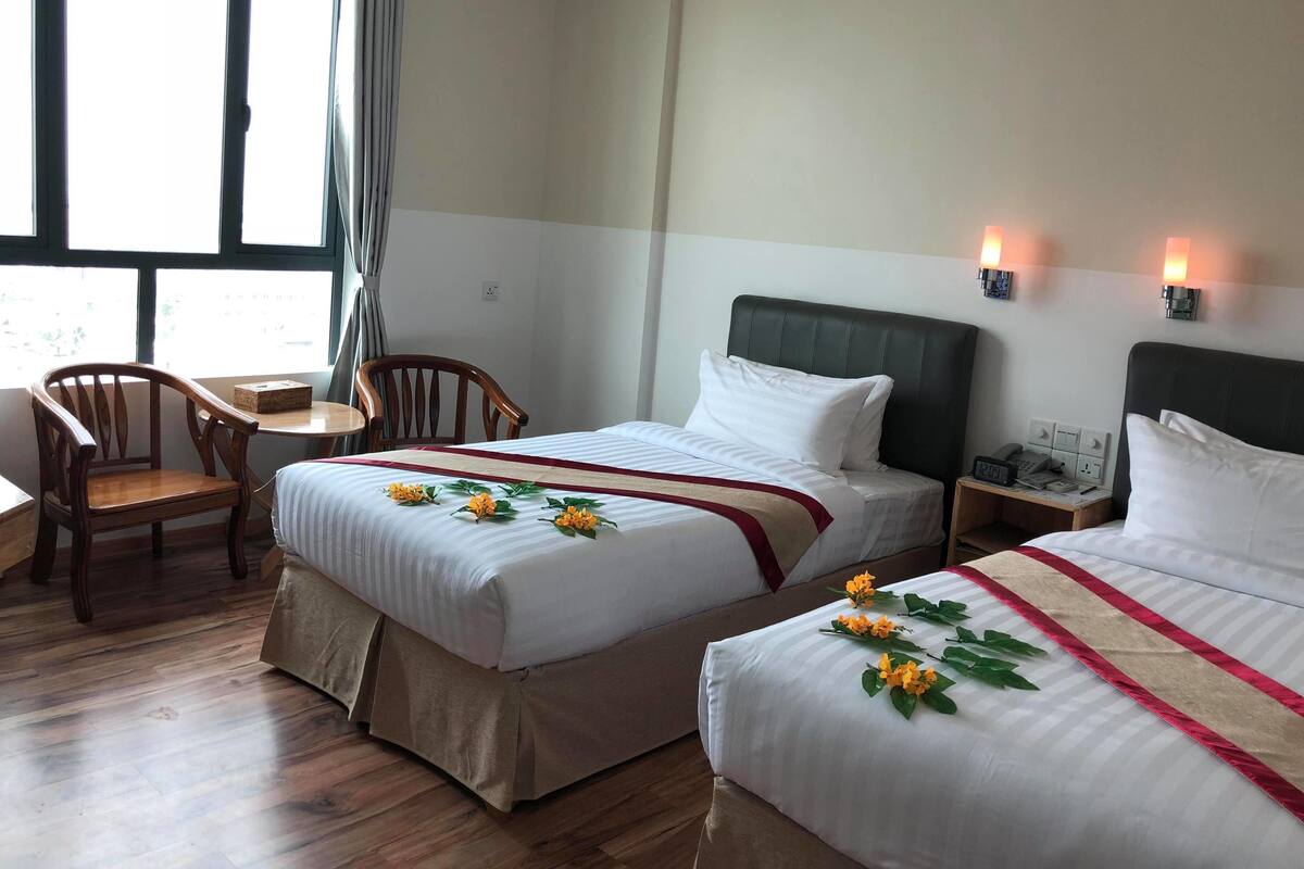 A hotel room with two beds, a wooden chair, a small table, and a nightstand with a phone and lamp.