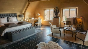 A bedroom with a large bed, a desk, and a chair. There is a window with curtains, a lamp, and a statue. - Boutique Hotel De Brakelhoen (Brakel)