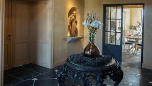 A spacious foyer with a large chandelier, a mounted deer head, a statue, and a table with a vase of flowers. - Boutique Hotel De Brakelhoen (Brakel)