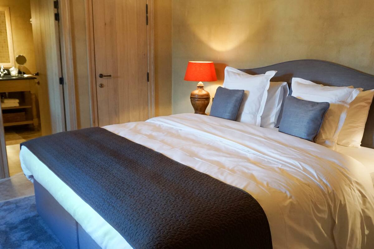 Una cama bien hecha con un edredón gris, un armario de madera y una lámpara de noche.