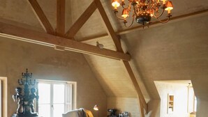 A cozy attic bedroom with a sloped ceiling, a chandelier, a bed with a fluffy rug, and a small table with chairs. - Boutique Hotel De Brakelhoen (Brakel)