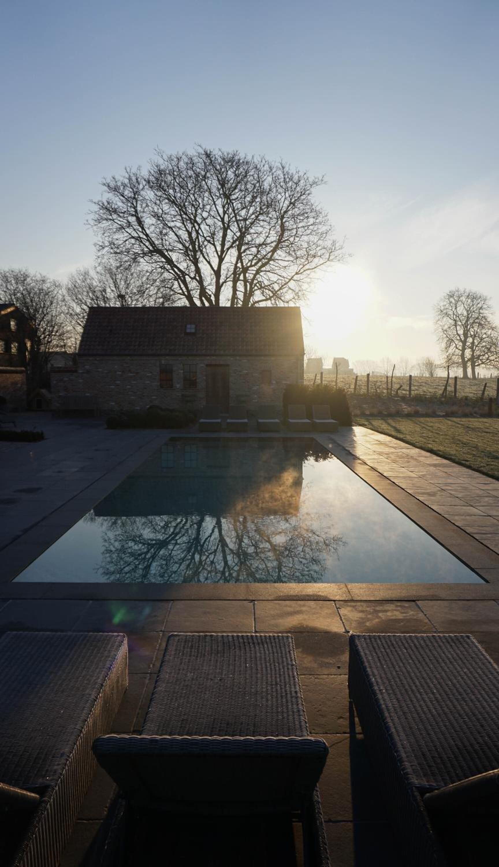 A swimming pool with lounge chairs in the foreground, a stone building in the background, and a clear sky.