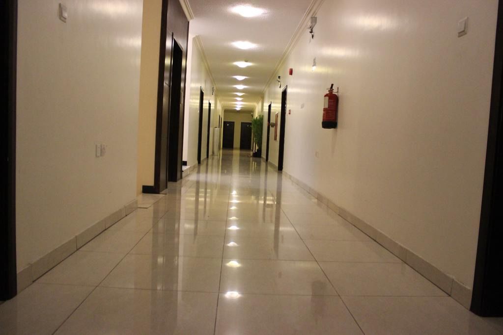 A long, well-lit hallway with a shiny tiled floor, doors on both sides, and a fire extinguisher mounted on the wall.