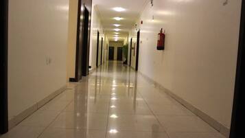 A long, well-lit hallway with a shiny tiled floor, doors on both sides, and a fire extinguisher mounted on the wall.
