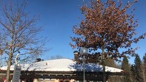 A building with a snow-covered roof, a signboard, and a tree with brown leaves. - Chiemgautraum (Siegsdorf)