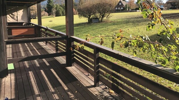 A wooden deck with a railing overlooking a grassy yard with trees and a house in the background. - Chiemgautraum (Siegsdorf)