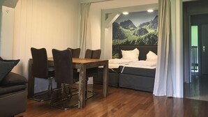 A room with a bed, a dining table with chairs, and a view of mountains through a window. - Chiemgautraum (Siegsdorf)