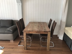 Ein Holztisch mit Metallstühlen, ein graues Sofa und ein Bett mit weißen Vorhängen.