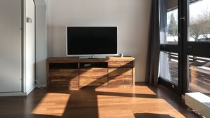 A modern living room with a flat-screen TV on a wooden console, large windows, and a sliding glass door. - Chiemgautraum (Siegsdorf)