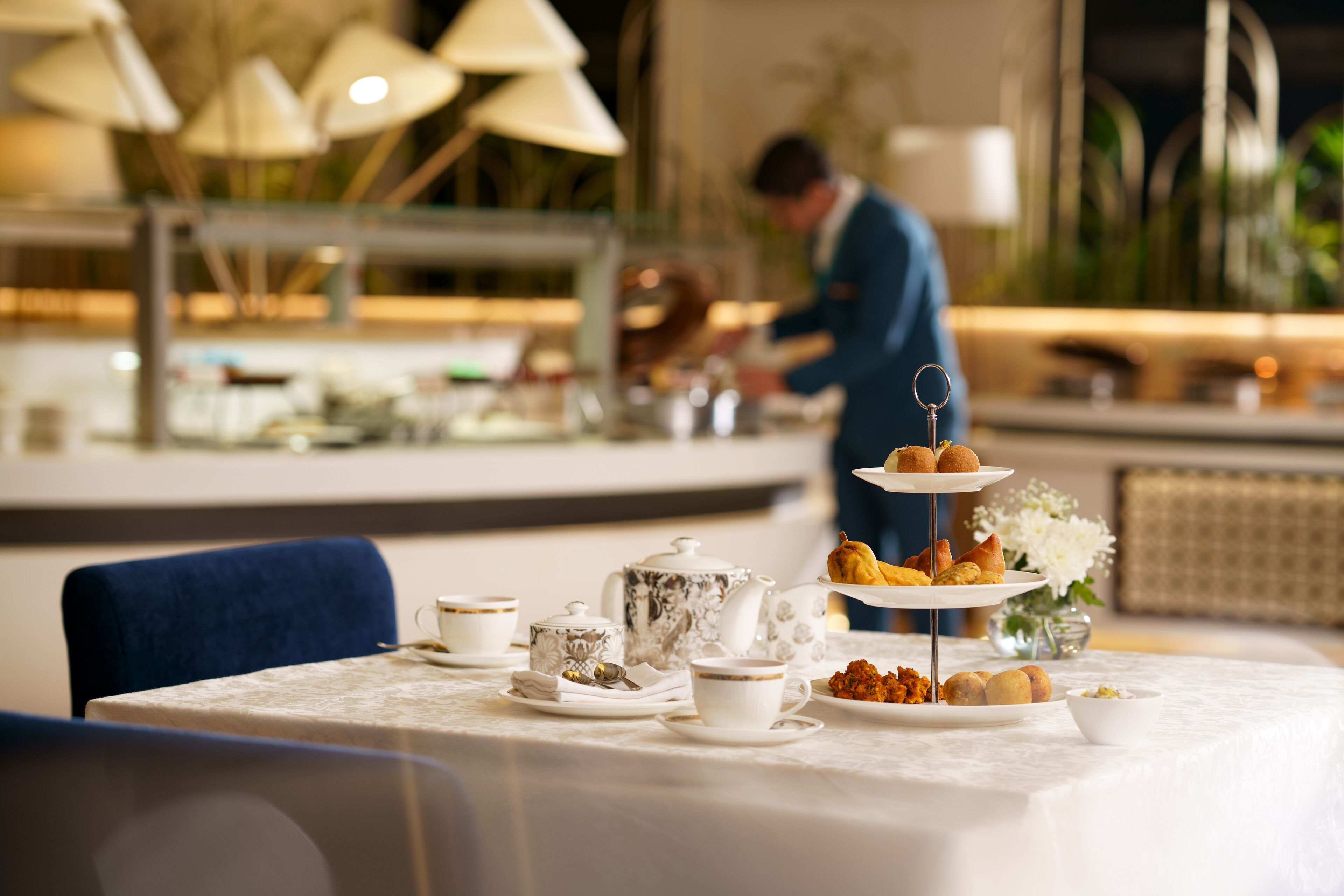 A dining table set with tea service, pastries, and a tiered dessert display in a restaurant.