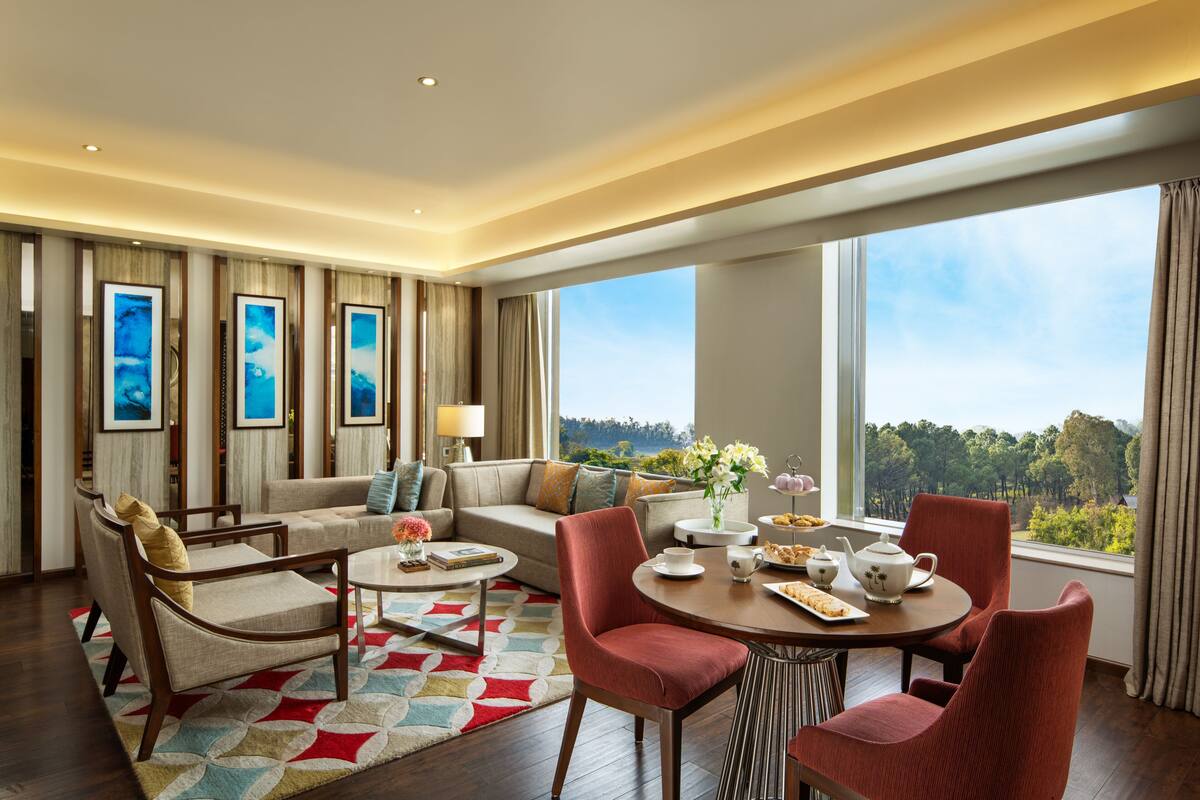 Una habitación de hotel moderna con un ventanal grande, un sofá, una mesa de comedor y una mesa de centro.