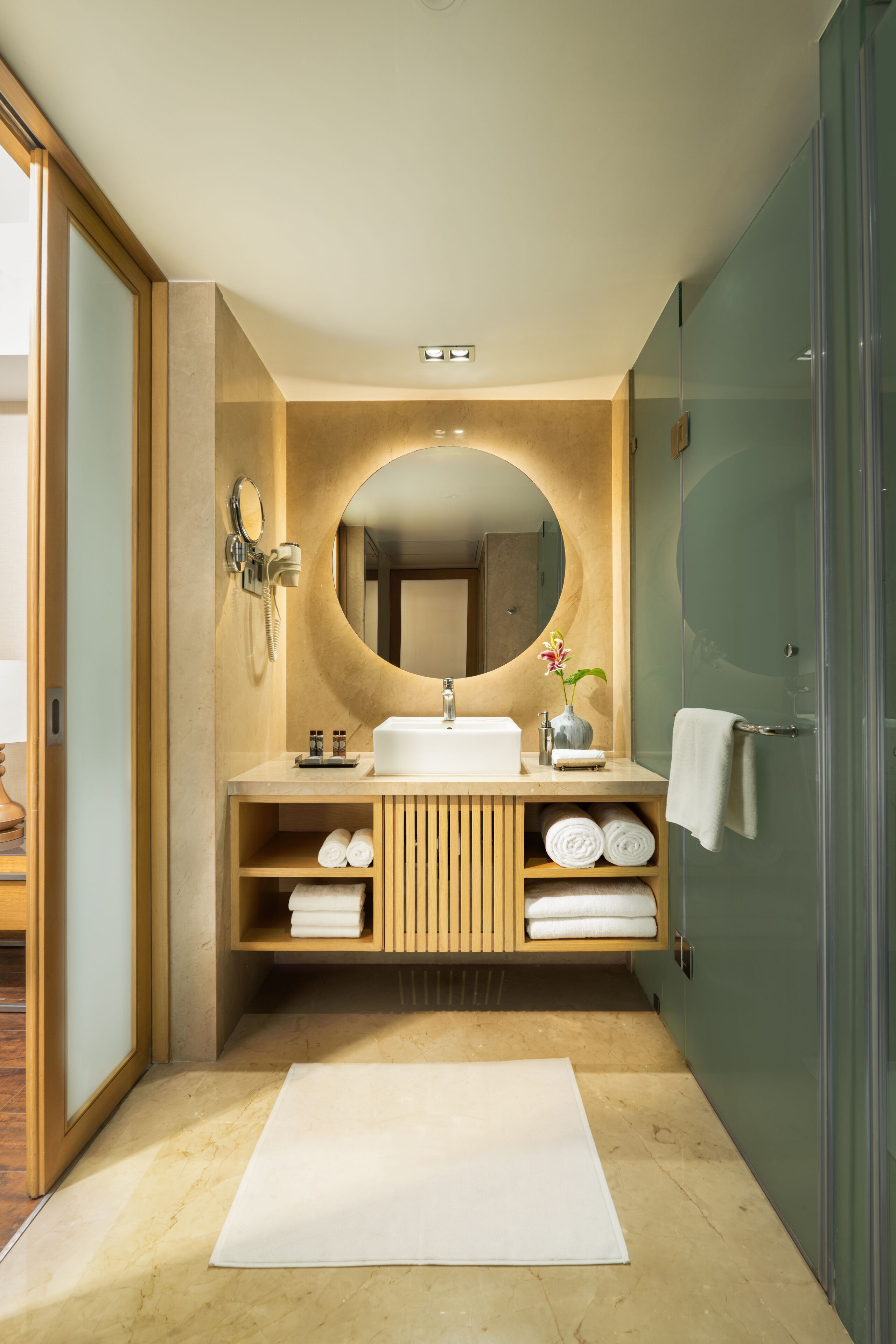 Un baño moderno con tocador de madera, un espejo redondo, un lavabo y una cabina de ducha de vidrio.