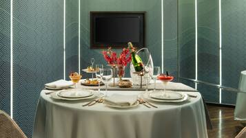 A dining area with a round table set for four, a television mounted on the wall, and a patterned wallpaper.
