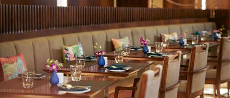 Un restaurant avec des tables et des chaises en bois, un banc rembourré et des centres de table ornés de fleurs.