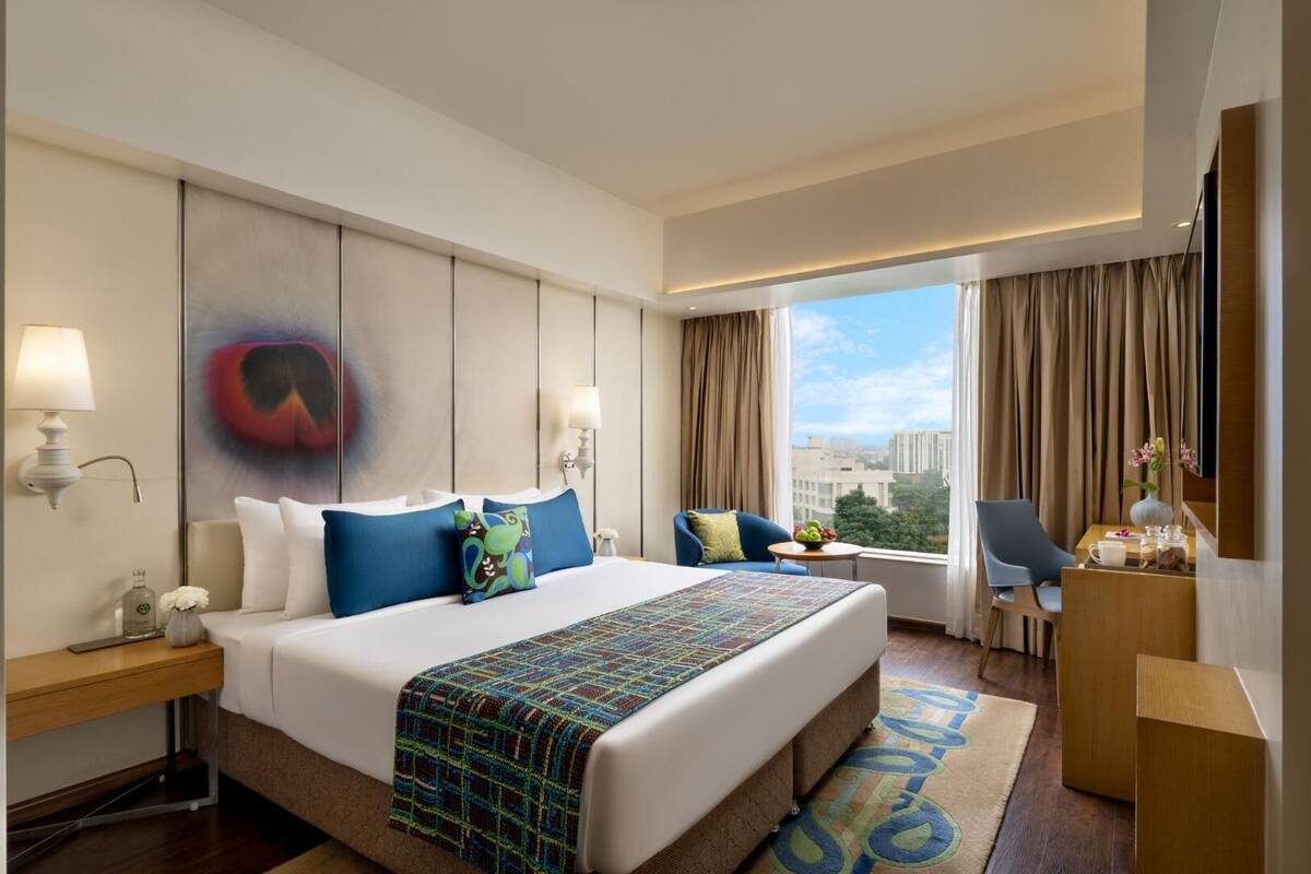 Habitación de hotel con una cama grande, un escritorio, una silla, una ventana con cortinas y vistas a la ciudad.