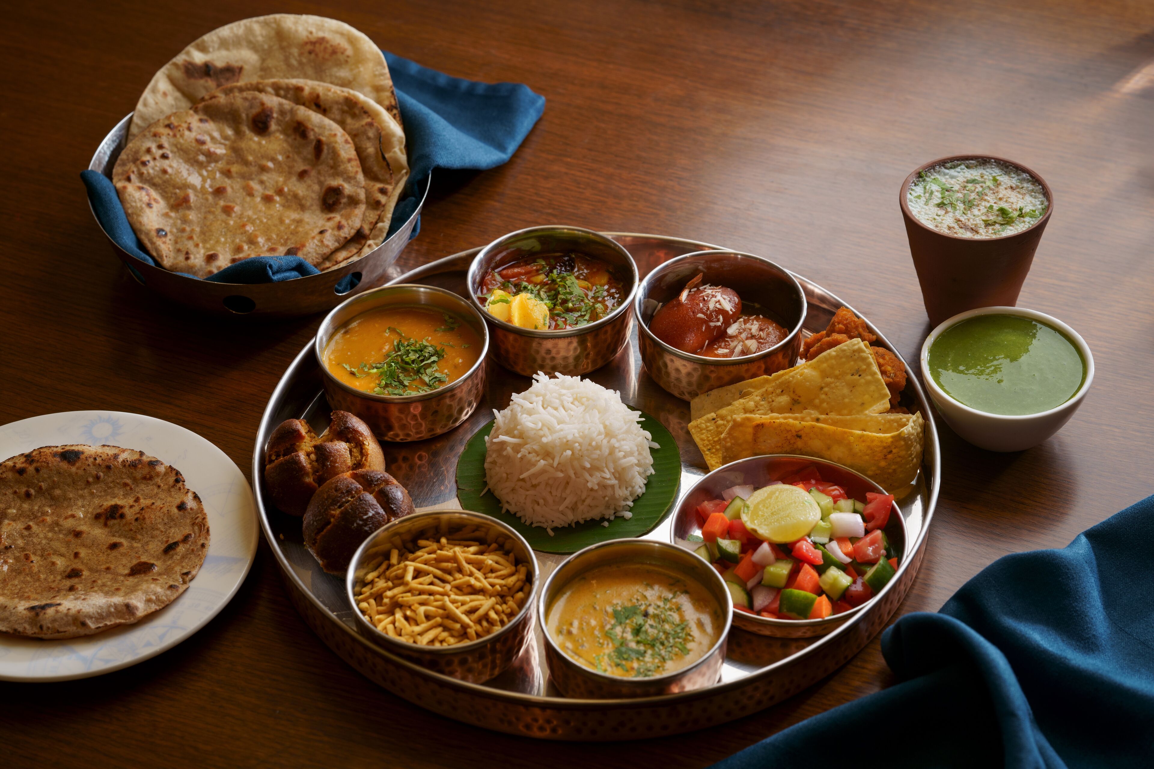 Una comida tradicional india con varios platos sobre una bandeja de metal, incluyendo arroz, curry y panes planos.