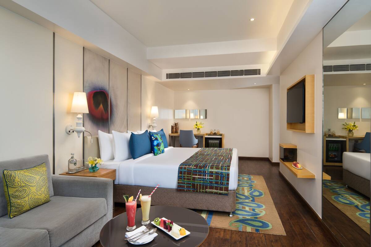 Una habitación de hotel con cama, sofá, una mesa de centro con bebidas y televisión.