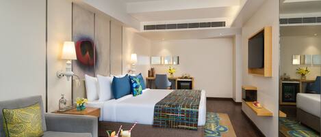 A hotel room with a bed, a sofa, a coffee table with drinks, and a TV.