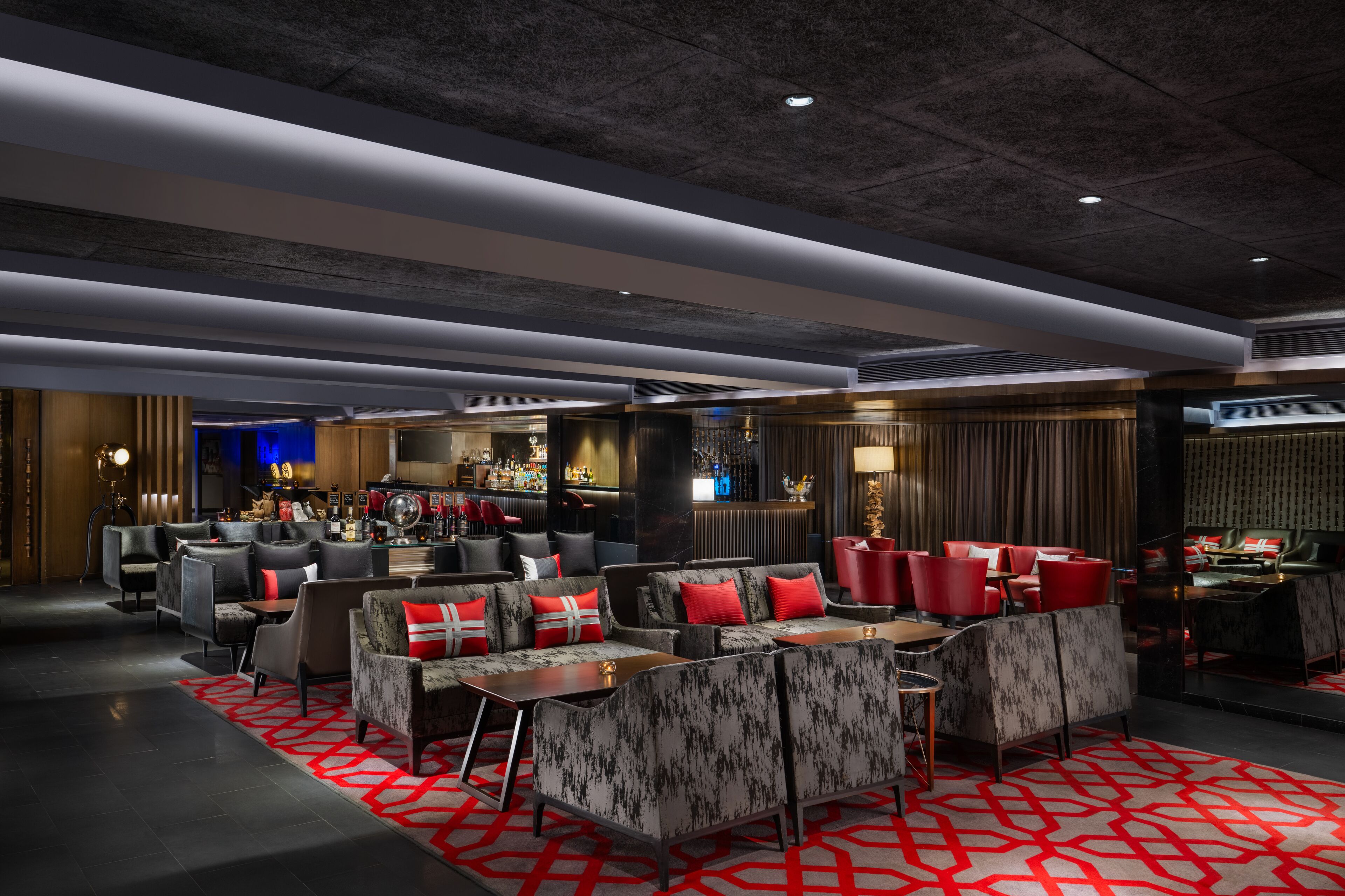 A modern lounge area with sofas and armchairs, a bar, and a seating area with a patterned carpet.
