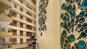 A multi-level hotel lobby with a central seating area, a decorative wall art installation, and a modern architectural design. - Wow Crest, Indore – IHCL SeleQtions (Indore)